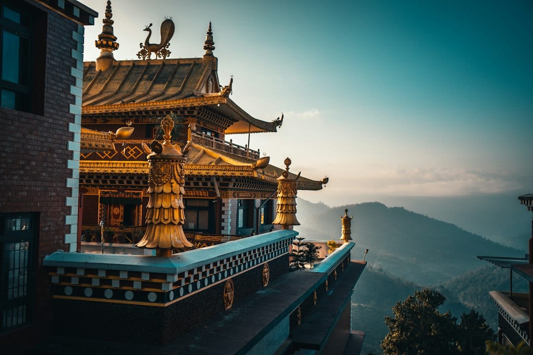 A golden Buddhist monastery roof with ornate finials overlooking misty mountain ridges at dawn