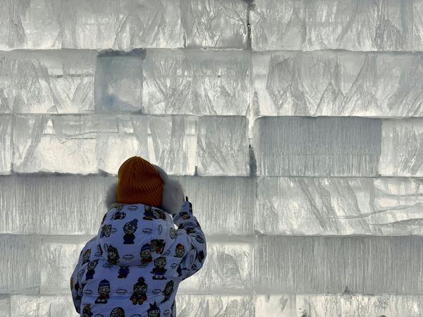 A person standing in front of a wall of ice at Harbin Ice Festival